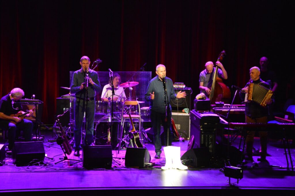 Hudební skupina hrající na pódiu s fialovým osvětlením.