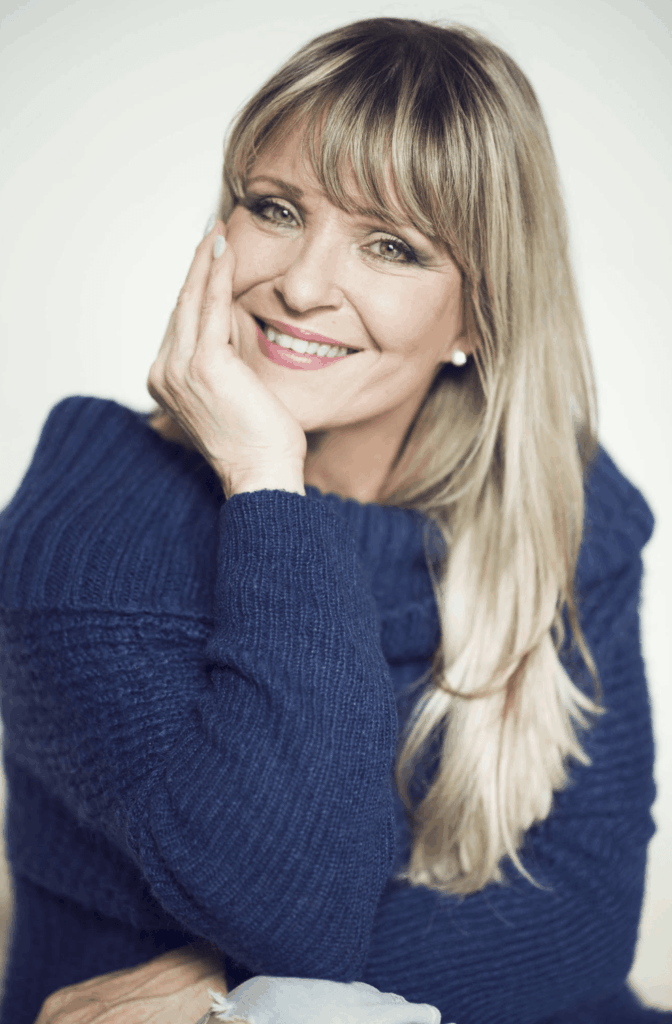 Portrét usmívající se herečky a zpěvačky Chantal Poullain v modrém pleteném svetru.