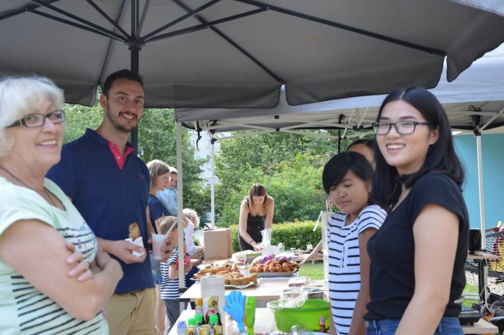 Skupina lidí pod stanem na venkovní komunitní akci.