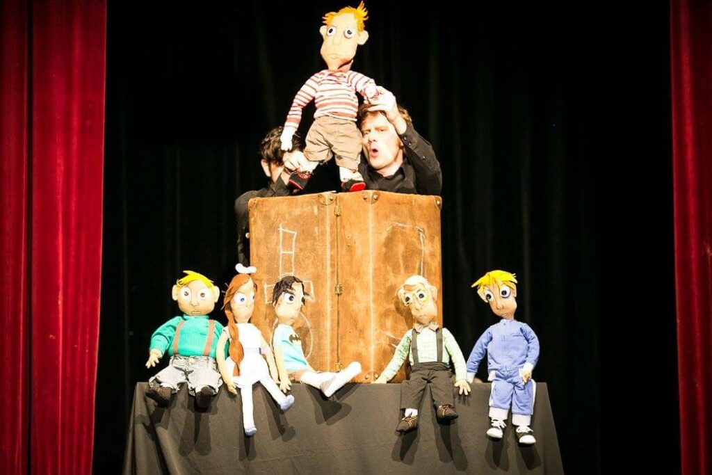 Loutkoherec hrající divadlo s několika loutkami na scéně.